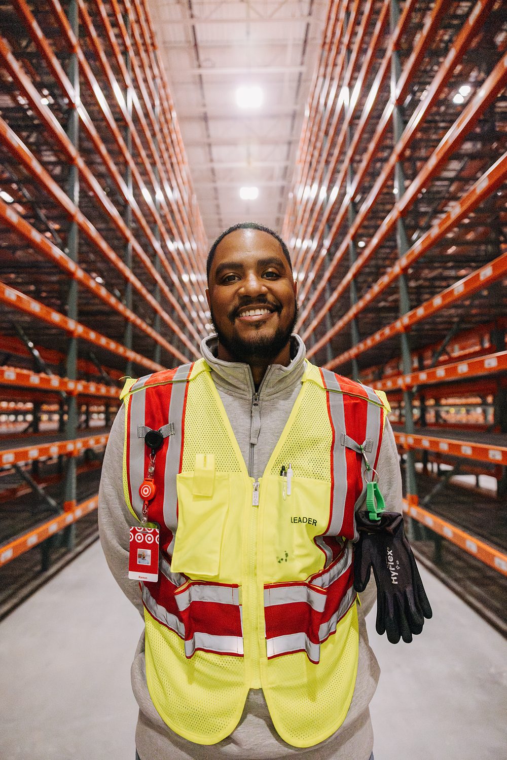 A warehouse worker in a high-visibility vest photographed between storage racks.