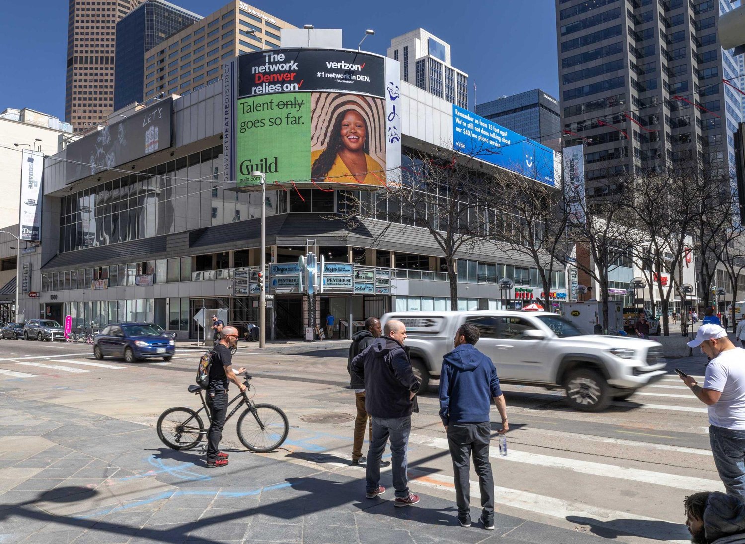 Digital out-of-home screens on a downtown street corner carrying the rebranded Guild creative.