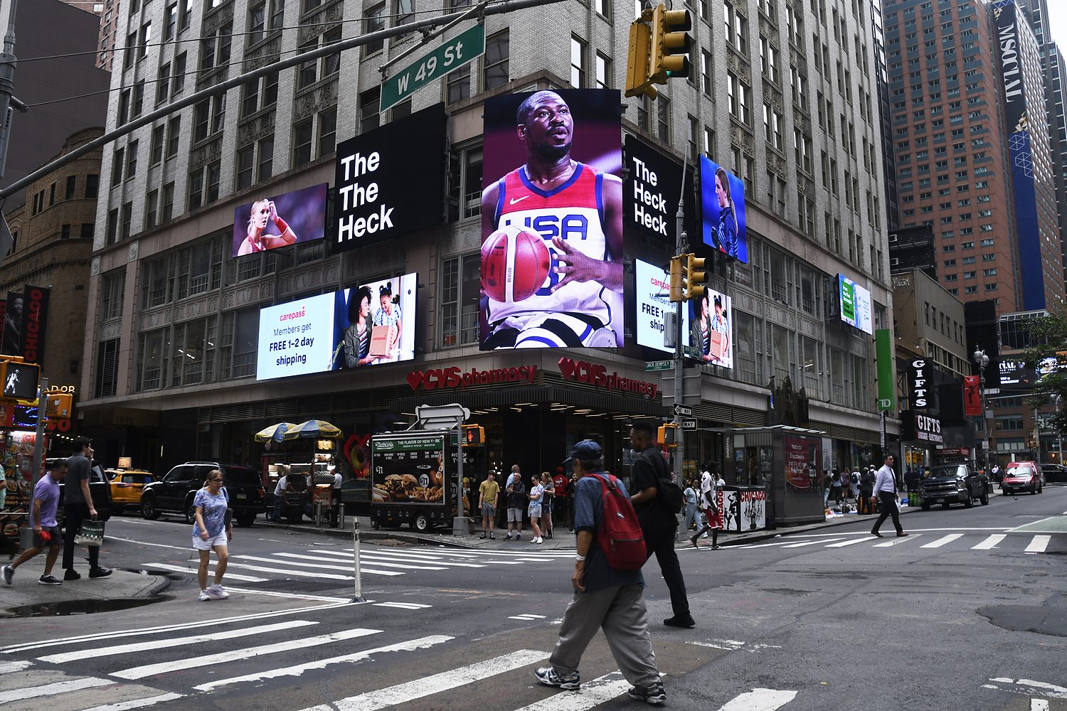 Digital screens on the Brill Building at West 49th Street reading The Heck, with a Team USA basketball athlete.
